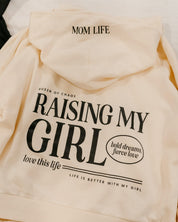 Hoodie in bone with black 'Raising My Girl' graphic on flat lay - Little Mama Shirt Shop