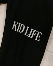 Joggers close up leg view in black with white 'Kid Life' graphic on flat lay- Little Mama Shirt Shop