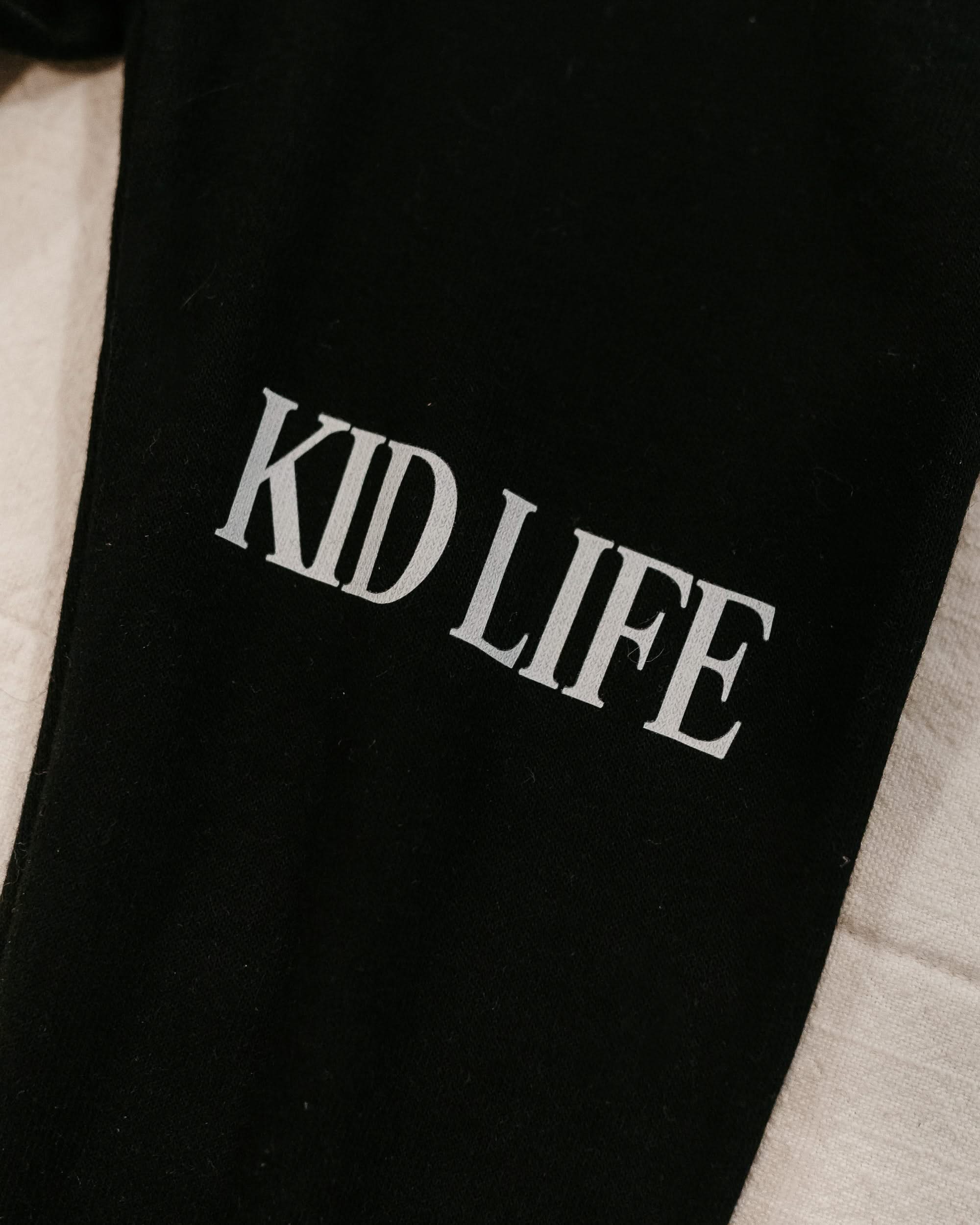 Joggers close up leg view in black with white 'Kid Life' graphic on flat lay- Little Mama Shirt Shop