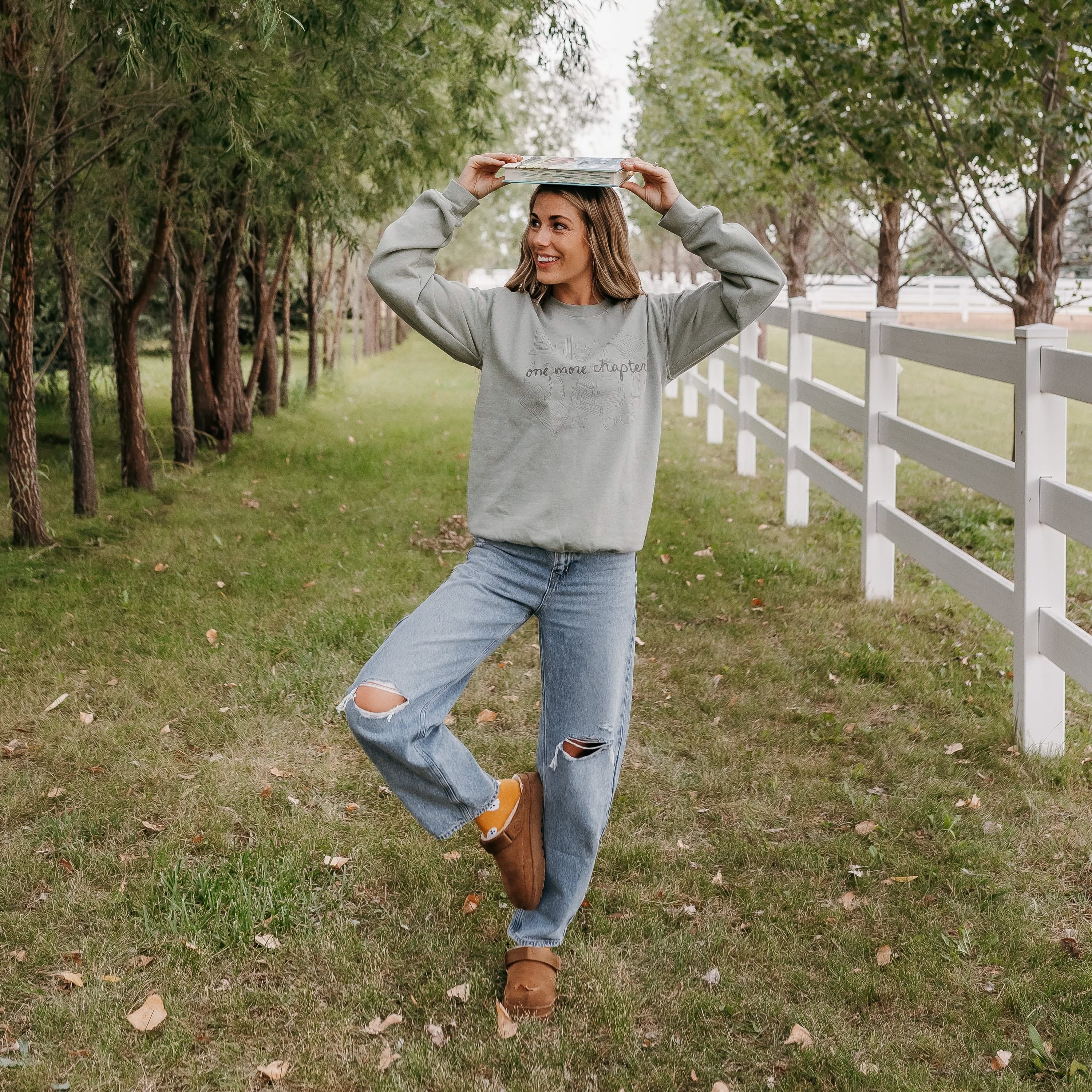 Unisex “One More Chapter” crewneck in sage with cozy tone on tone book lover illustration, on model – Little Mama Shirt Shop