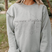 Unisex “One More Chapter” crewneck in sage with cozy tone on tone book lover illustration, on model – Little Mama Shirt Shop