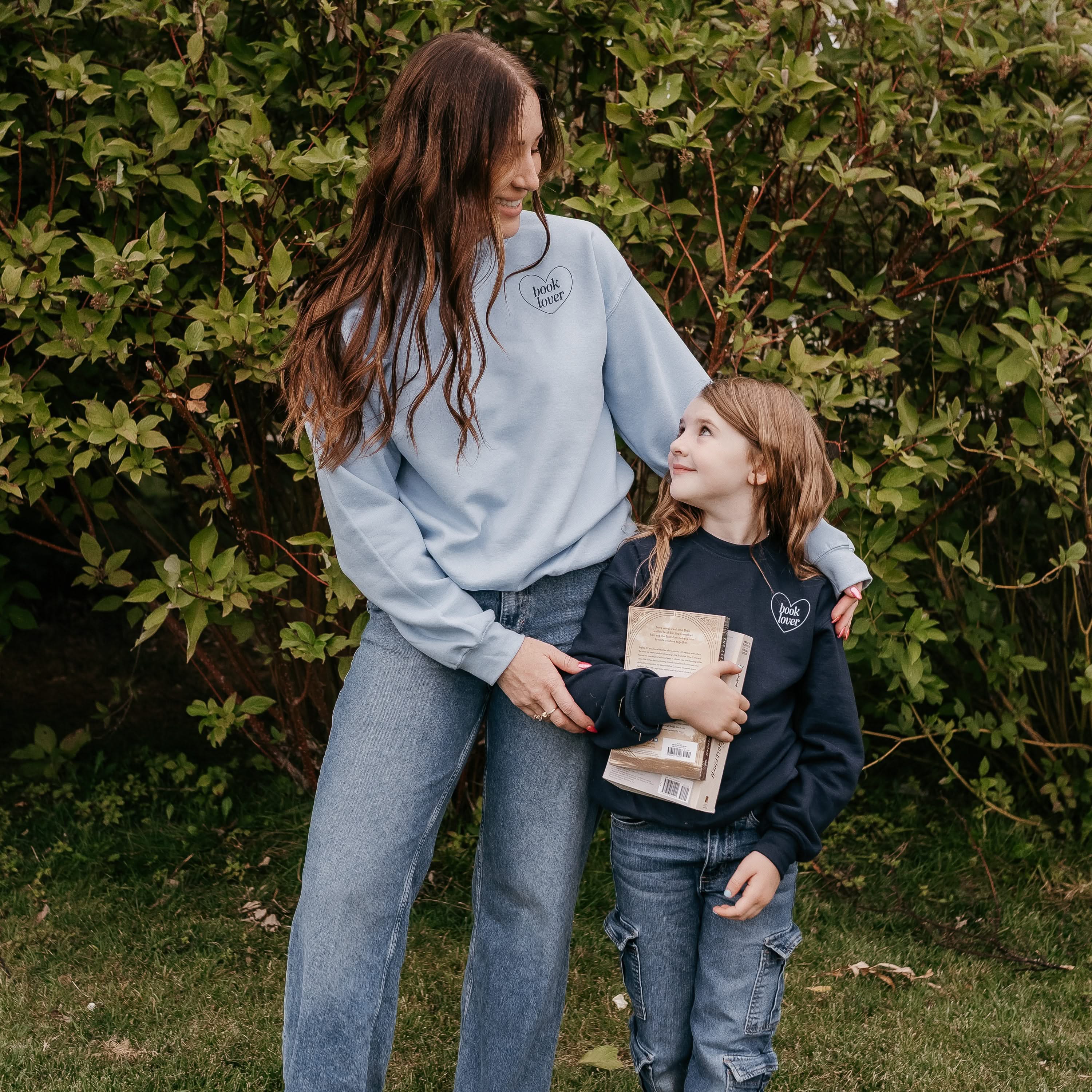 Set of two coordinating fleece sweaters for book lovers: an adult light blue sweater with navy “Book Lover” text, paired with a child’s navy sweater with light blue “Book Lover” text, displayed on side by side models - Little Mama Shirt Shop