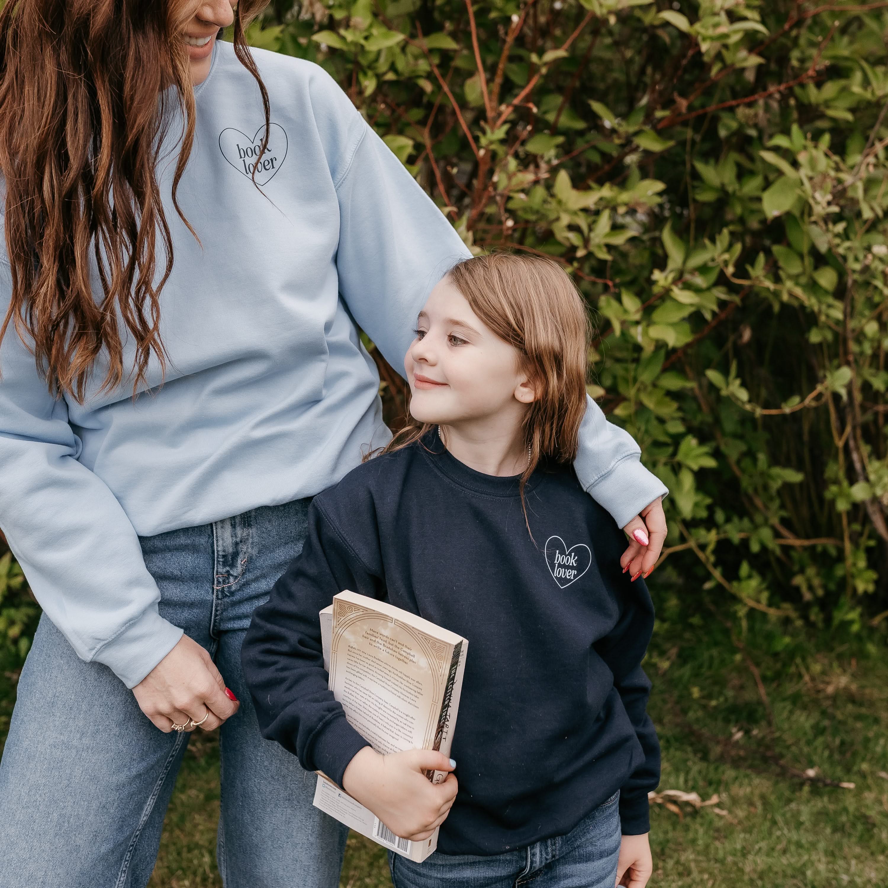 Set of two coordinating fleece sweaters for book lovers: an adult light blue sweater with navy “Book Lover” text, paired with a child’s navy sweater with light blue "Book Lover" text, displayed on side by side models - Little Mama Shirt Shop
