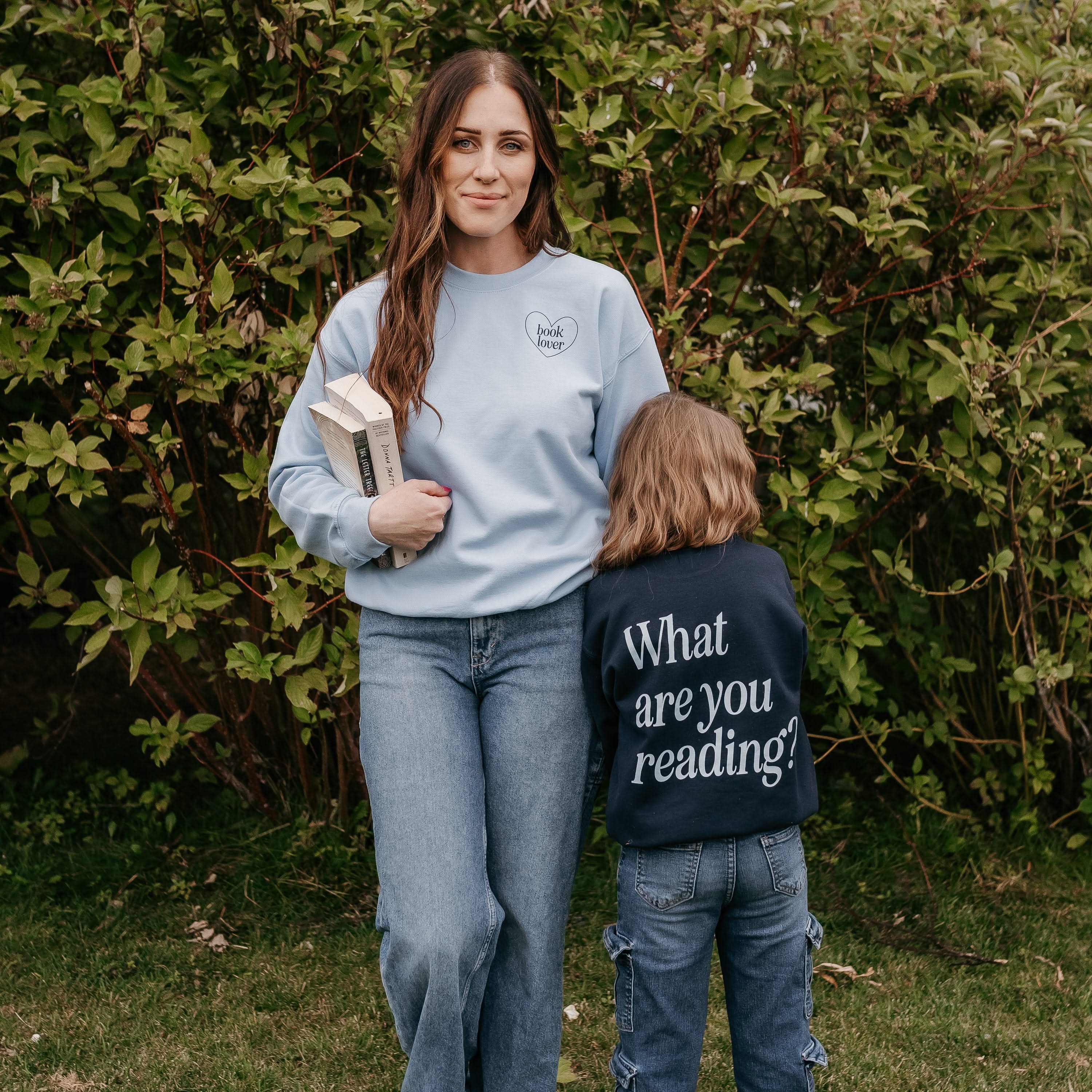 Set of two coordinating fleece sweaters for book lovers: an adult light blue sweater with navy “Book Lover” text, paired with a child’s navy sweater with light blue “What Are You Reading?” text, displayed on side by side models - Little Mama Shirt Shop