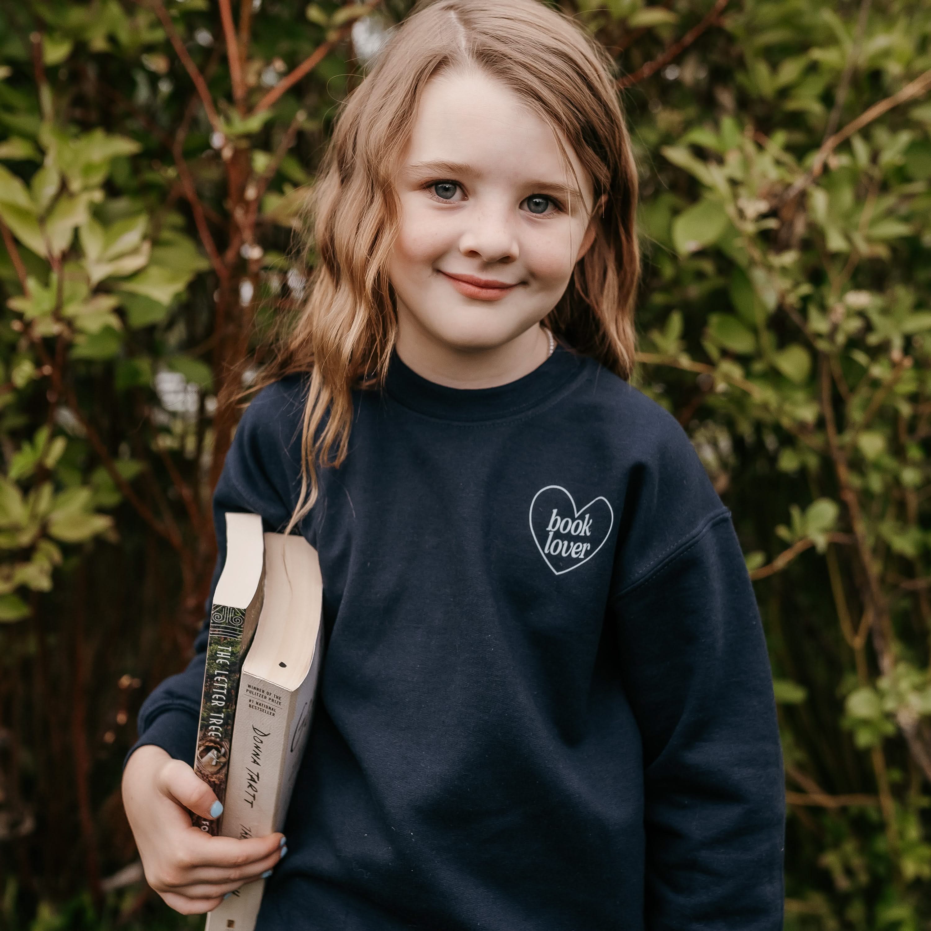 Child sweater in navy w/ light blue detail with a 'book lover' heart graphic on the front and 'What are you reading?' graphic on back, shown on model – Little Mama Shirt Shop