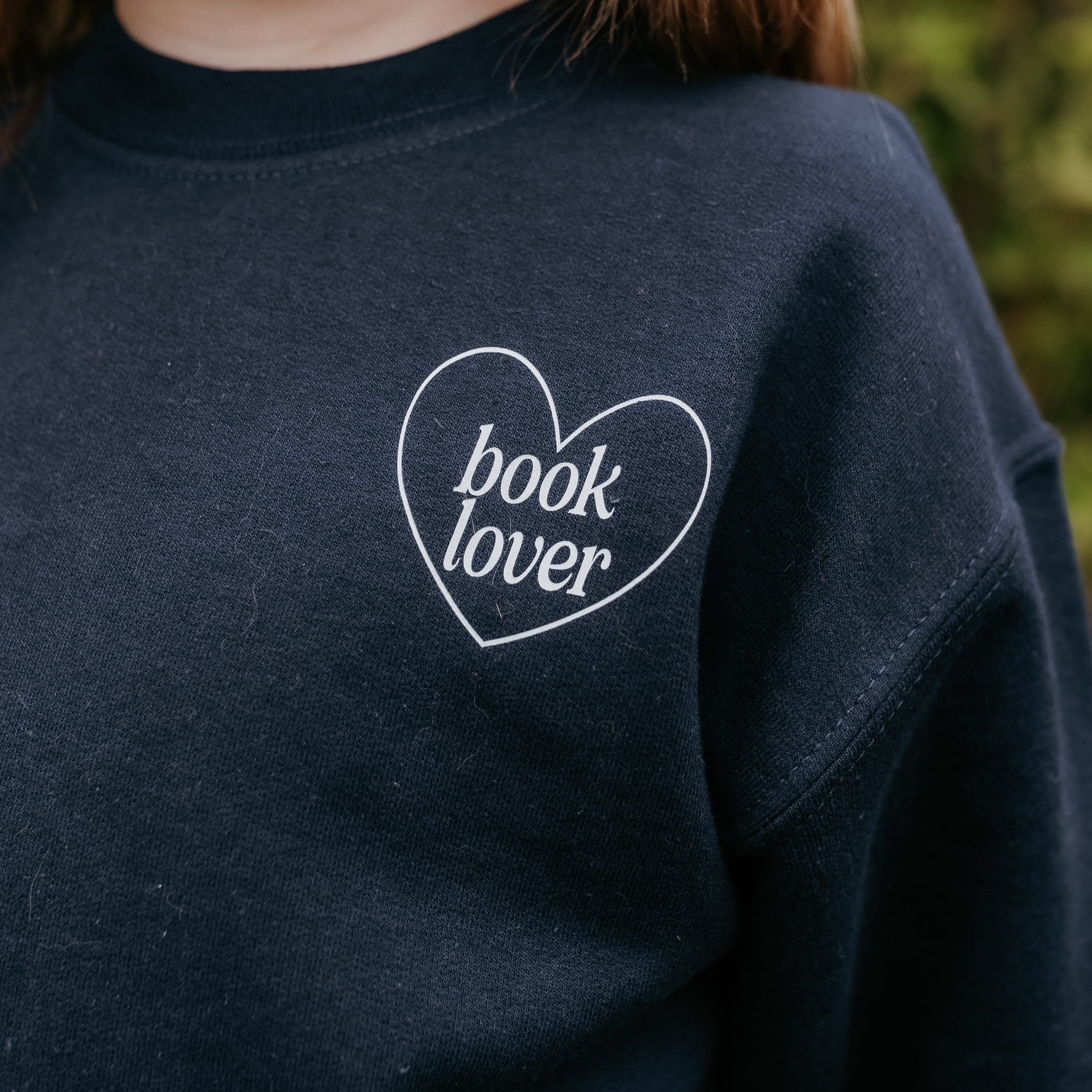 A child’s navy sweater with light blue “book lover” text in a heart, displayed on a model - Little Mama Shirt Shop