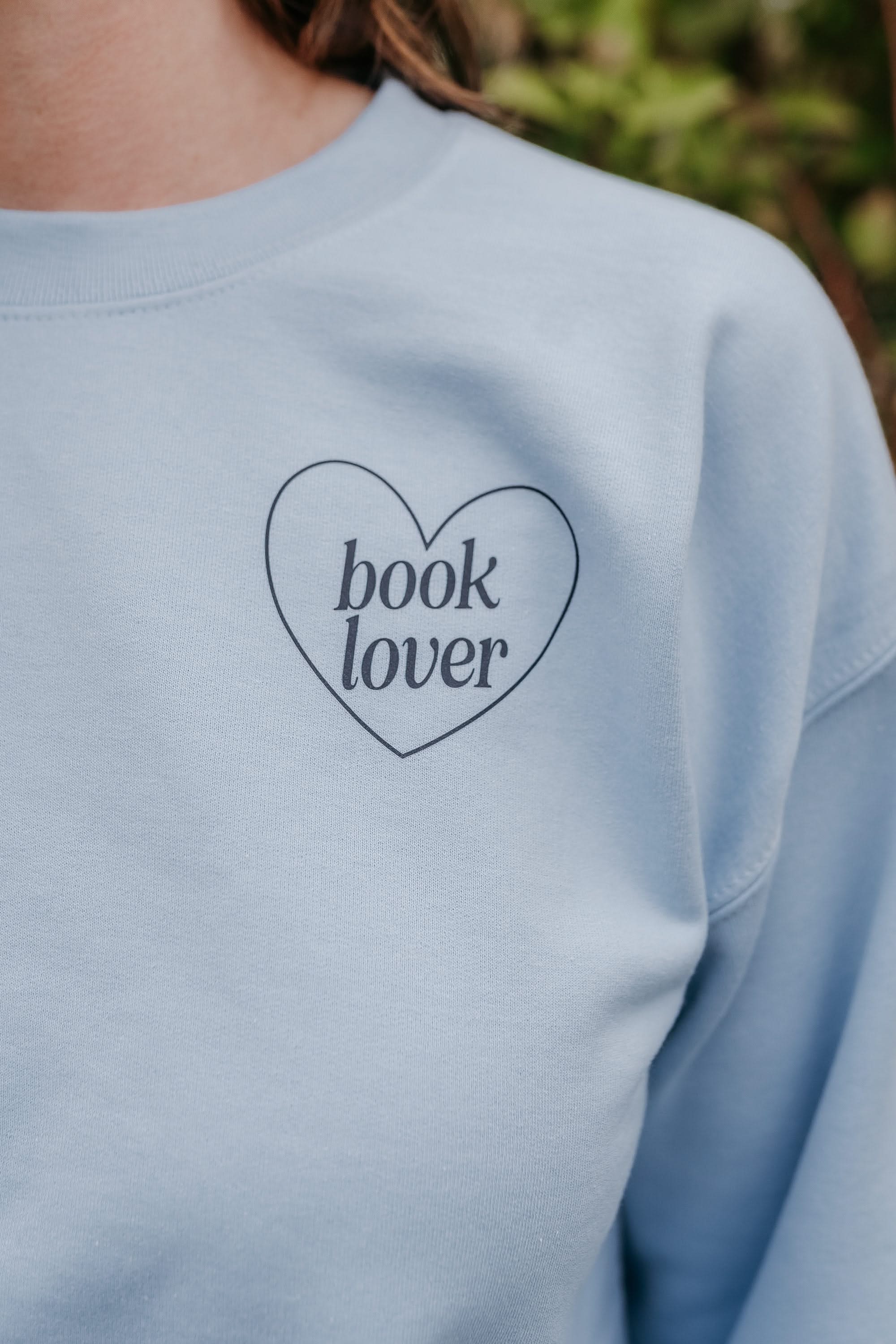 Adult light blue sweater with navy “Book Lover” text in heart, displayed on model - Little Mama Shirt Shop