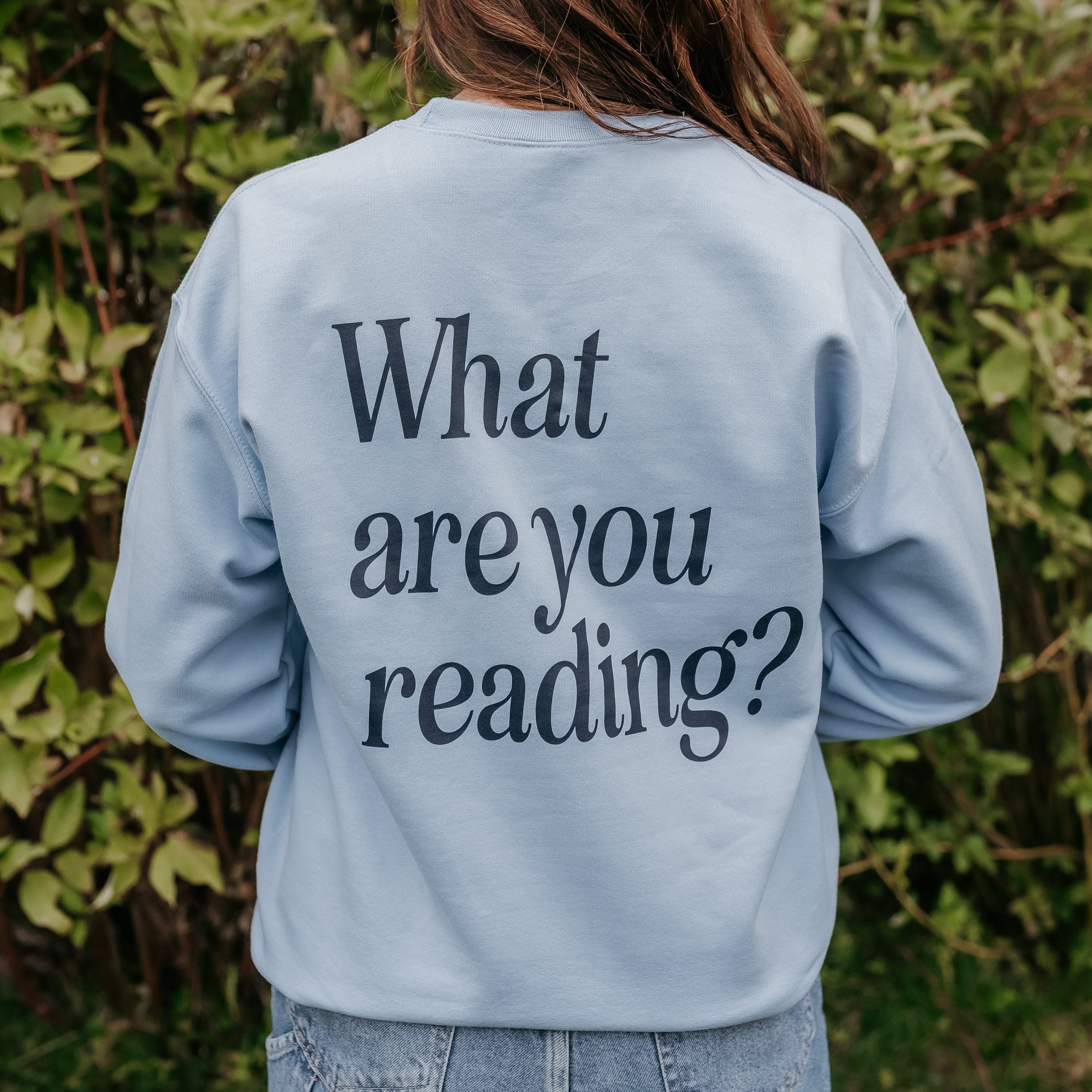 Adult light blue sweater with navy “What are you reading?" on back, displayed on model - Little Mama Shirt Shop