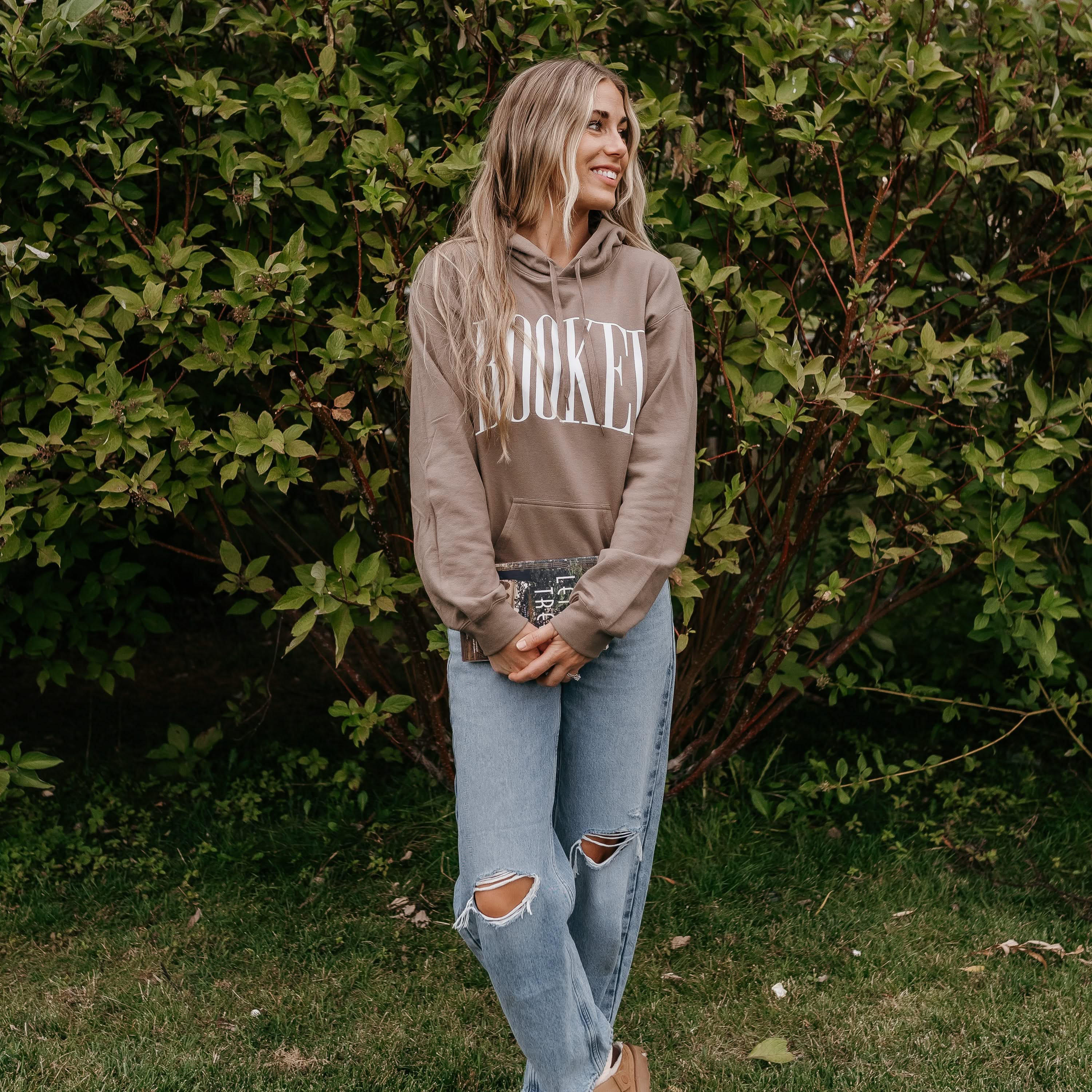 Unisex hoodie in brown savana with 'BOOKED' arched text on model – Little Mama Shirt Shop