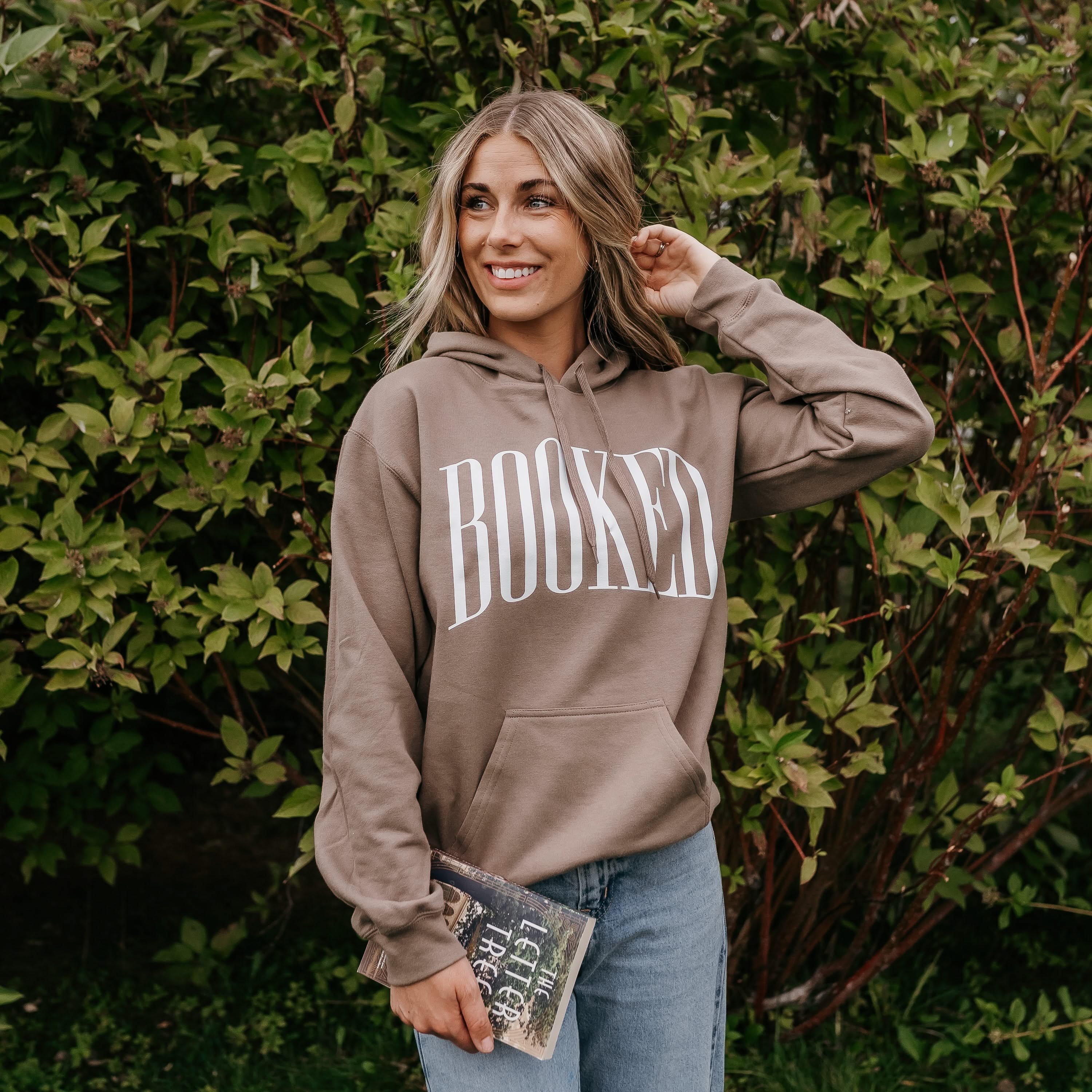 Unisex hoodie in brown savana with 'BOOKED' arched text on model – Little Mama Shirt Shop