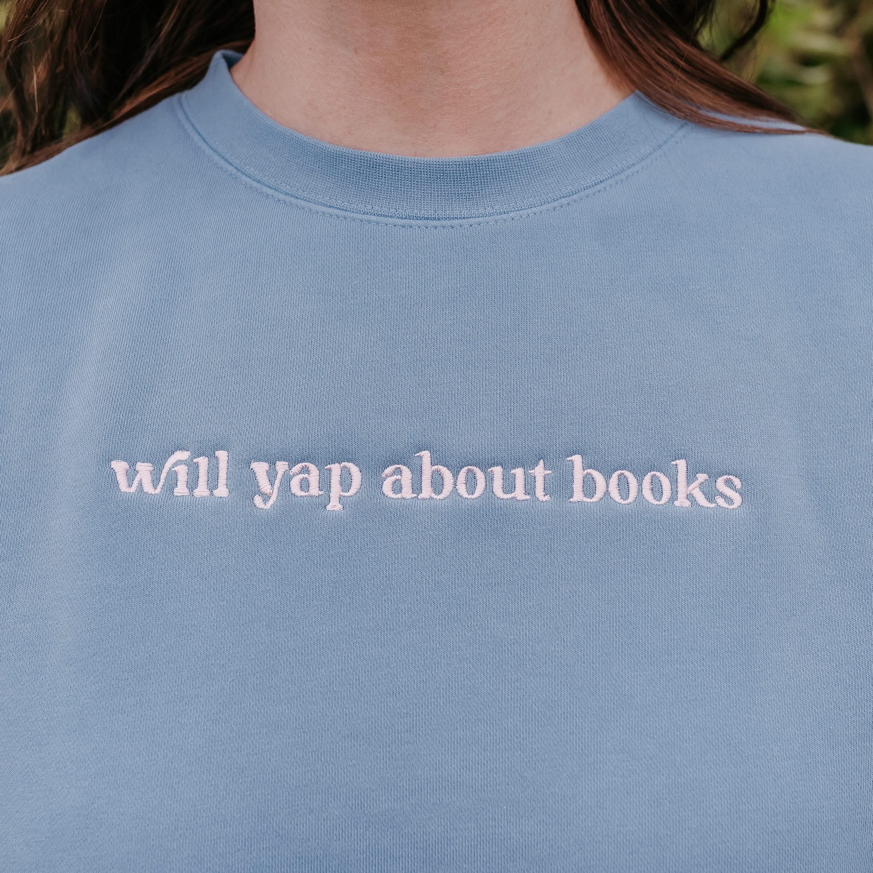 Embroidered “Will Yap About Books” pigment-dyed crewneck in light blue with pink thread on model  – Little Mama Shirt Shop