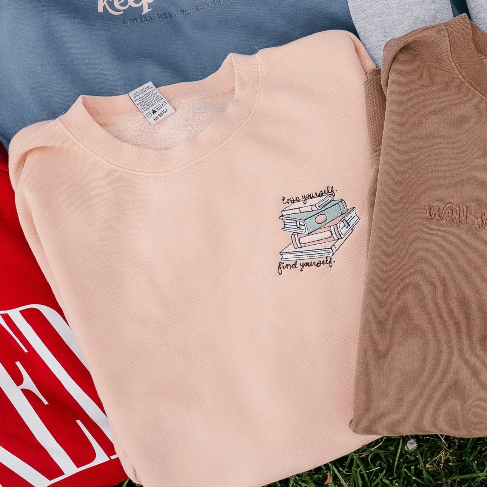 Unisex “Lose Yourself, Find Yourself” sweatshirt in pigment dusty pink with embroidered book stack on flat lay– Little Mama Shirt Shop