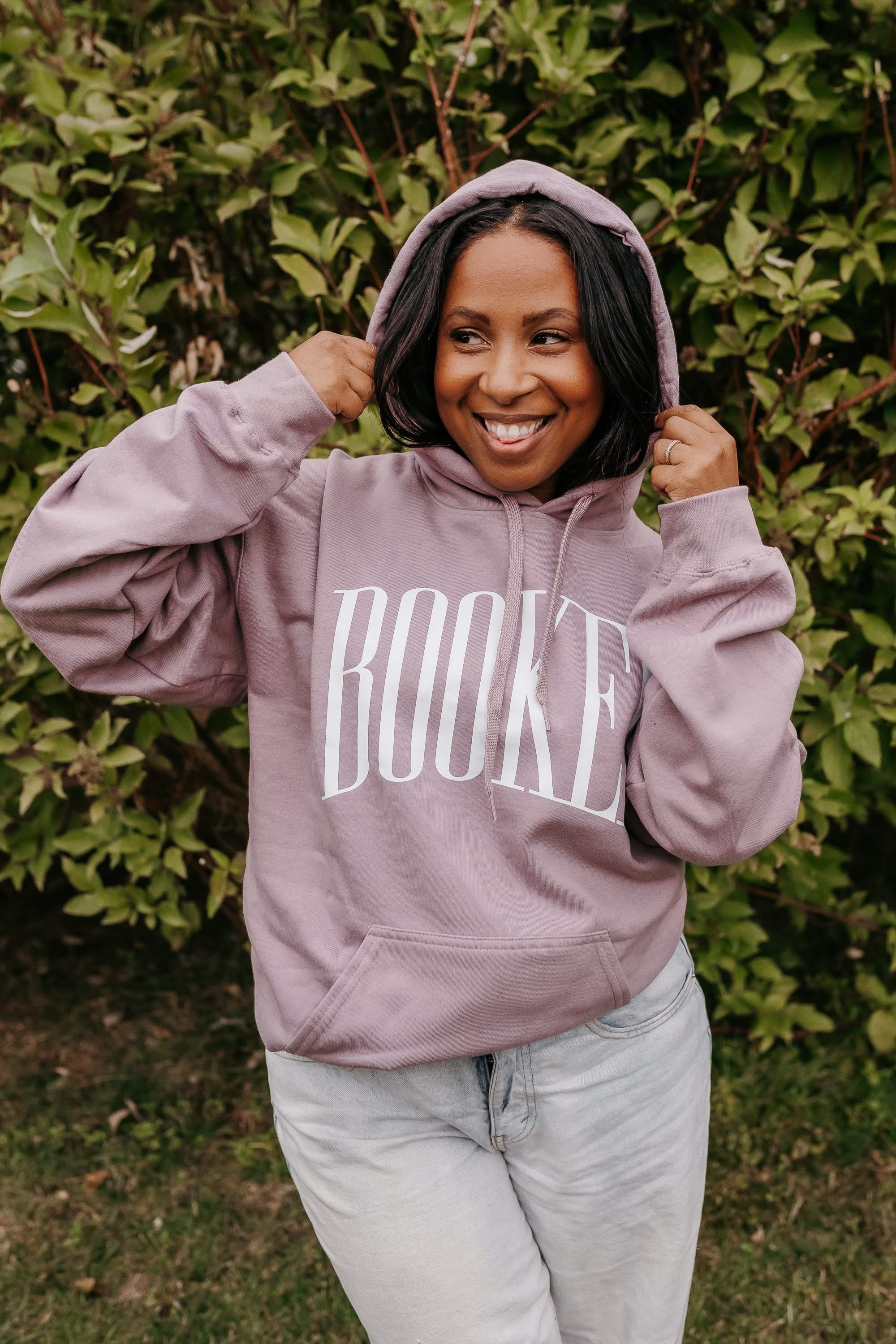 Unisex hoodie in paragon with 'BOOKED' arched text on model – Little Mama Shirt Shop