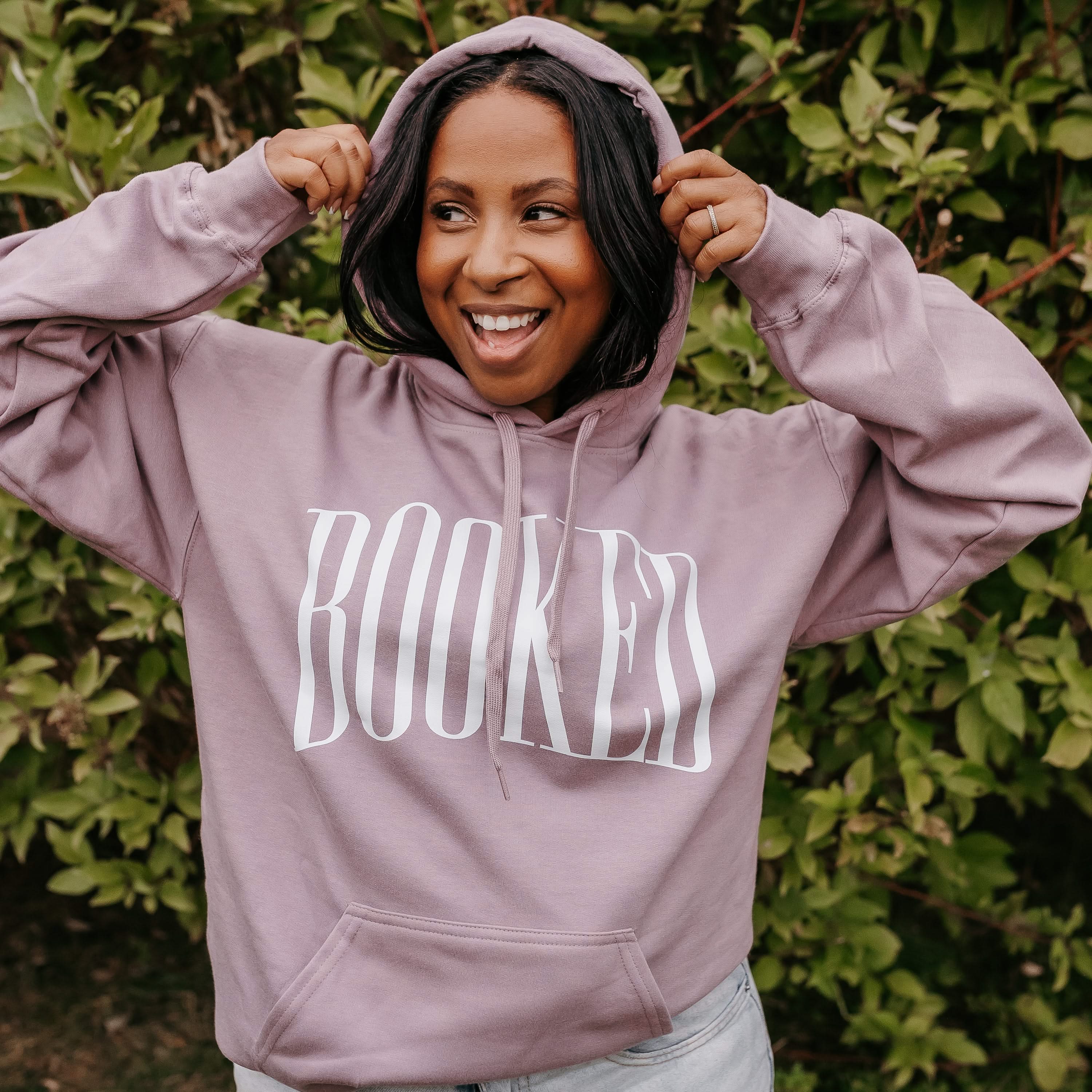 Unisex hoodie in paragon with 'BOOKED' arched text on model – Little Mama Shirt Shop