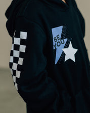 Child black sweater with checkers pattern on arm, and blue lightning bolt with 'be you' in it flanked by a white star, seen on model - Little Mama Shirt Shop