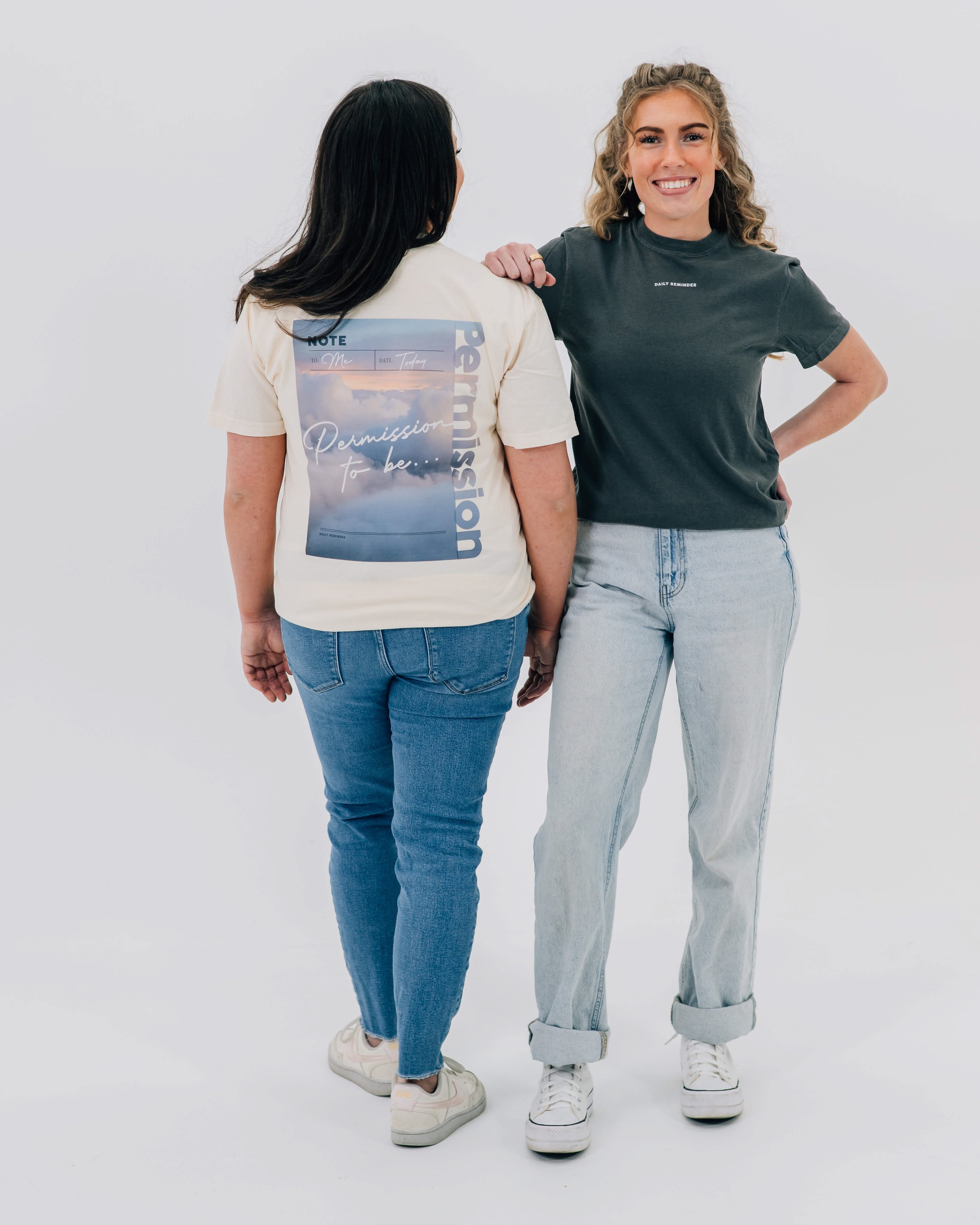 Ivory comfort colors tee with permission to be cloud graphic on back and pepper comfort colors tee with "daily reminder" printed on front, seen on models - Little Mama Shirt Shop