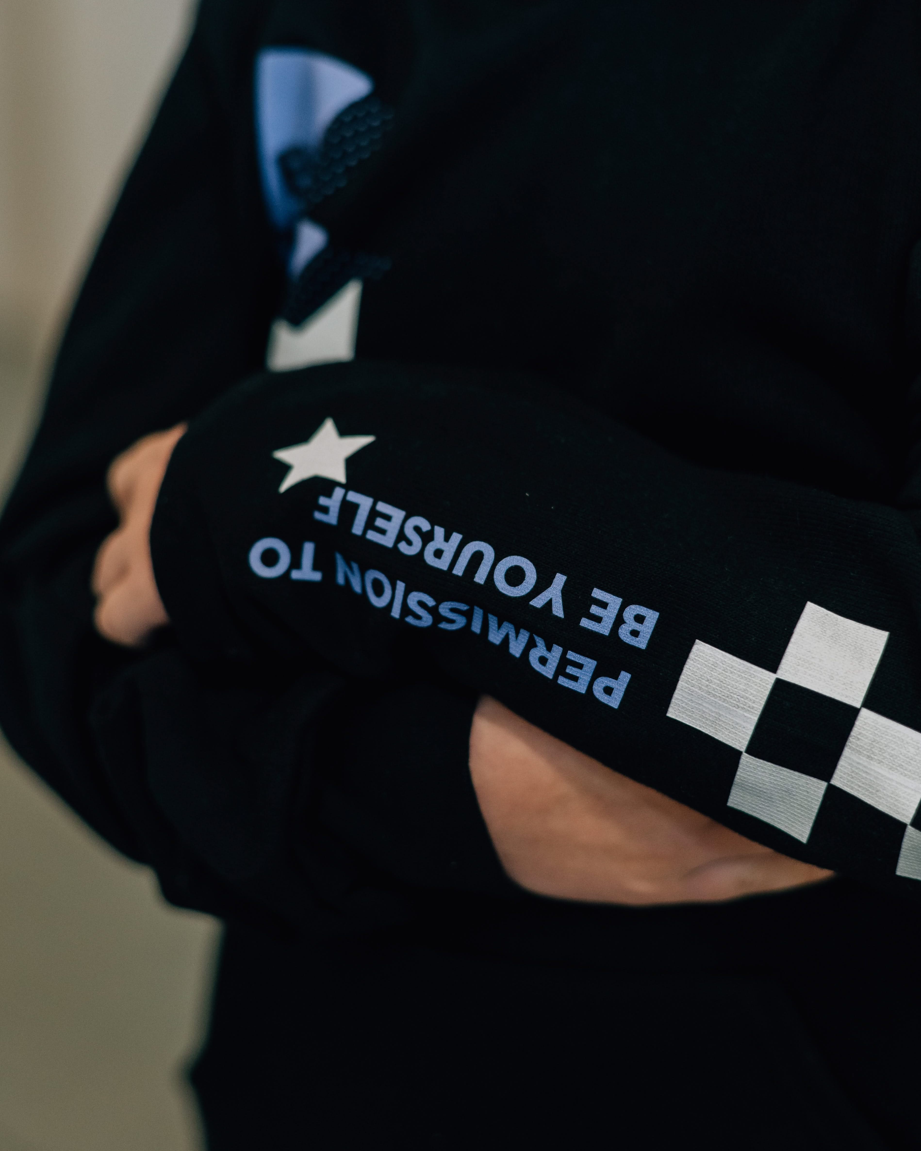 Child black sweater with checkers pattern on arm, and blue lightning bolt with 'be you' in it flanked by a white star, seen on model - Little Mama Shirt Shop