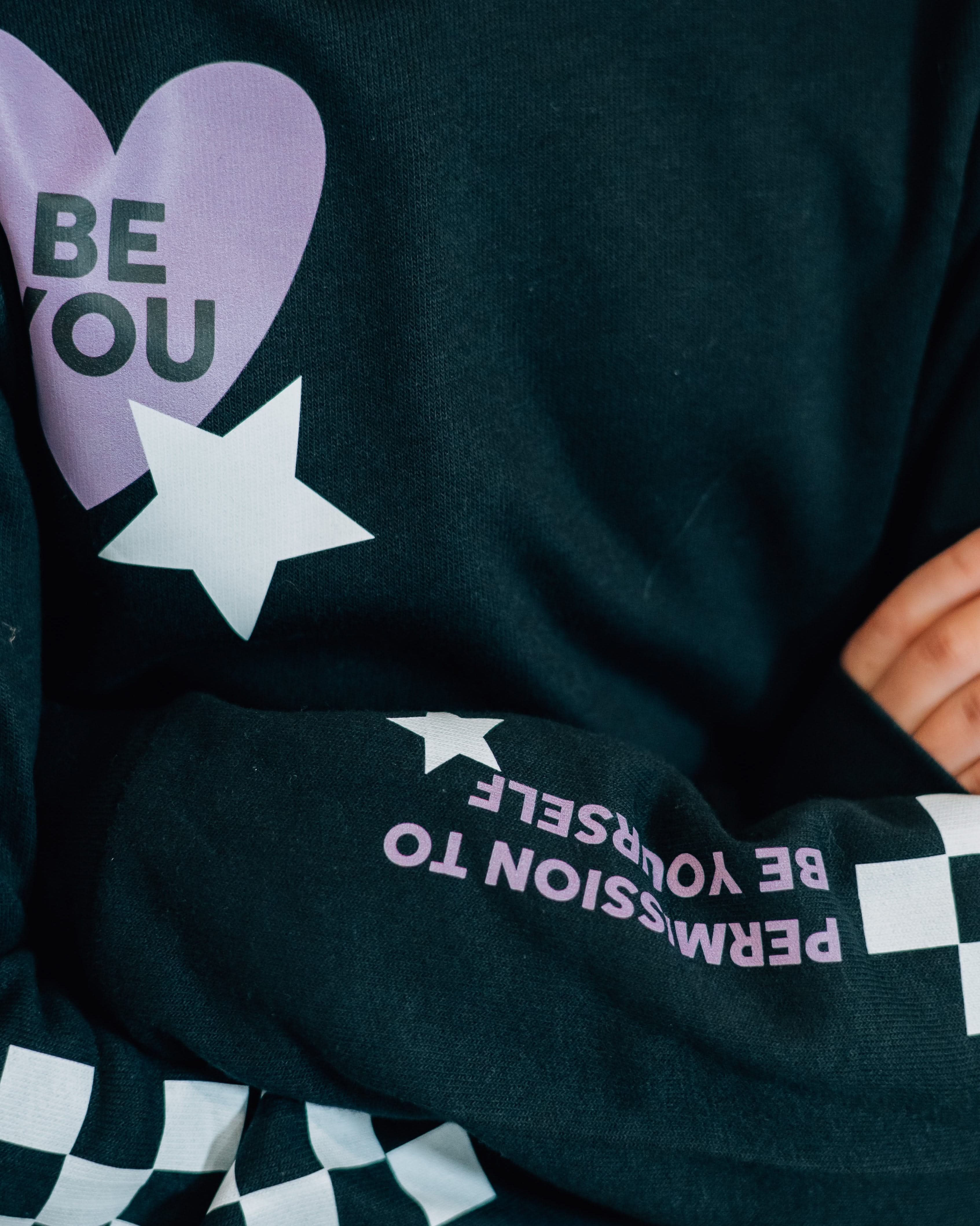 Child black sweater with checkers pattern on arm, and Purple Heart with 'be you' in it flanked by a white star, seen on model - Little Mama Shirt Shop