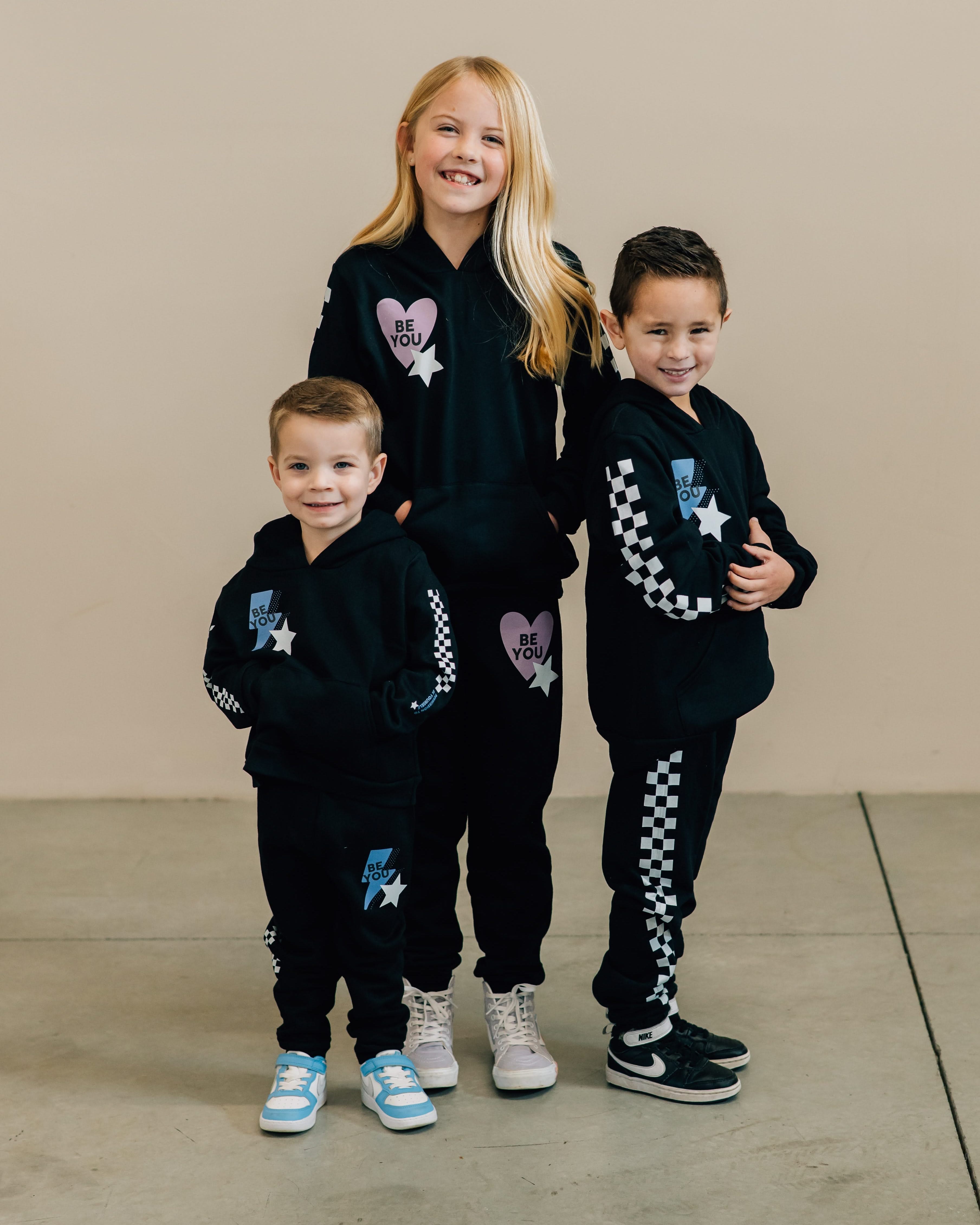 Child black sweater and joggers with checkers pattern on arm and leg, and Purple Heart or blue lightning bolt with 'be you' in it flanked by a white star, seen on models - Little Mama Shirt Shop