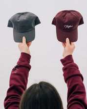 Gray hat with maroon and maroon hat with cream embroidery "Mother", model holding above head - Little Mama Shirt Shop