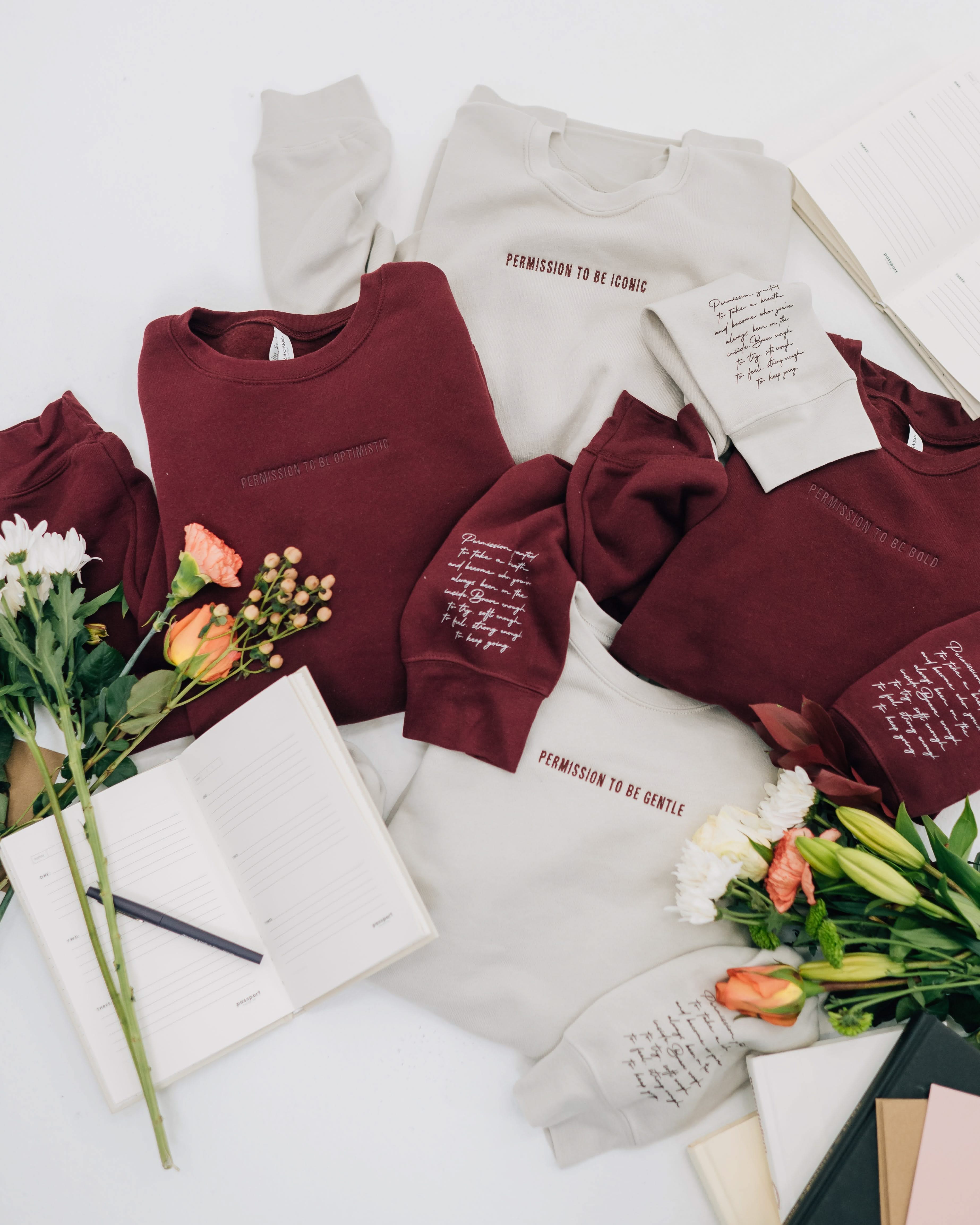 Maroon and dust crewnecks with "Permission To Be (Choose Your Word)" on chest and permission to be paragraph on sleeve, shown on flat lay - Little Mama Shirt Shop