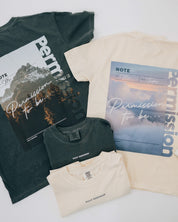 Ivory comfort colors tees with permission to be cloud graphic on back and 'daily reminder' on front and pepper comfort colors tee with permission to be mountain graphic on back and 'daily reminder' on front, seen on flat lay - Little Mama Shirt Shop