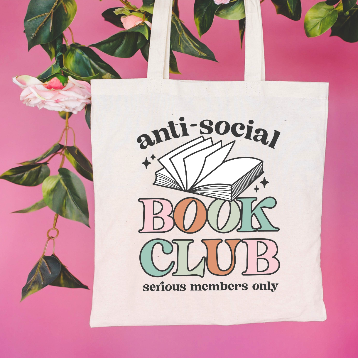 Beige canvas tote bag featuring a 'anti-social book club' design on a flat lay - Little Mama Shirt Shop