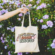 Beige canvas tote bag featuring a 'Don't Judge me by my Book Covers' design on a flat lay - Little Mama Shirt Shop