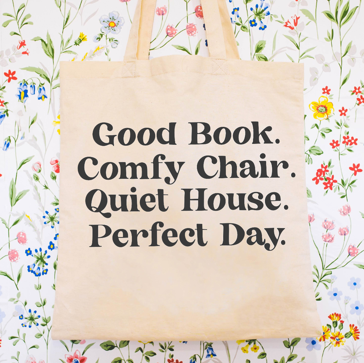 Beige canvas tote bag featuring a 'Good Book. Comfy Chair. Quiet House. Perfect Day.' design on a flat lay - Little Mama Shirt Shop