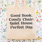 Beige canvas tote bag featuring a 'Good Book. Comfy Chair. Quiet House. Perfect Day.' design on a flat lay - Little Mama Shirt Shop