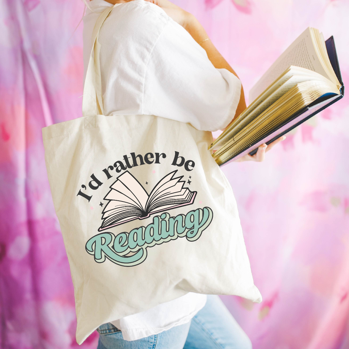 Beige canvas tote bag featuring a 'I'd rather be reading' design on a model - Little Mama Shirt Shop