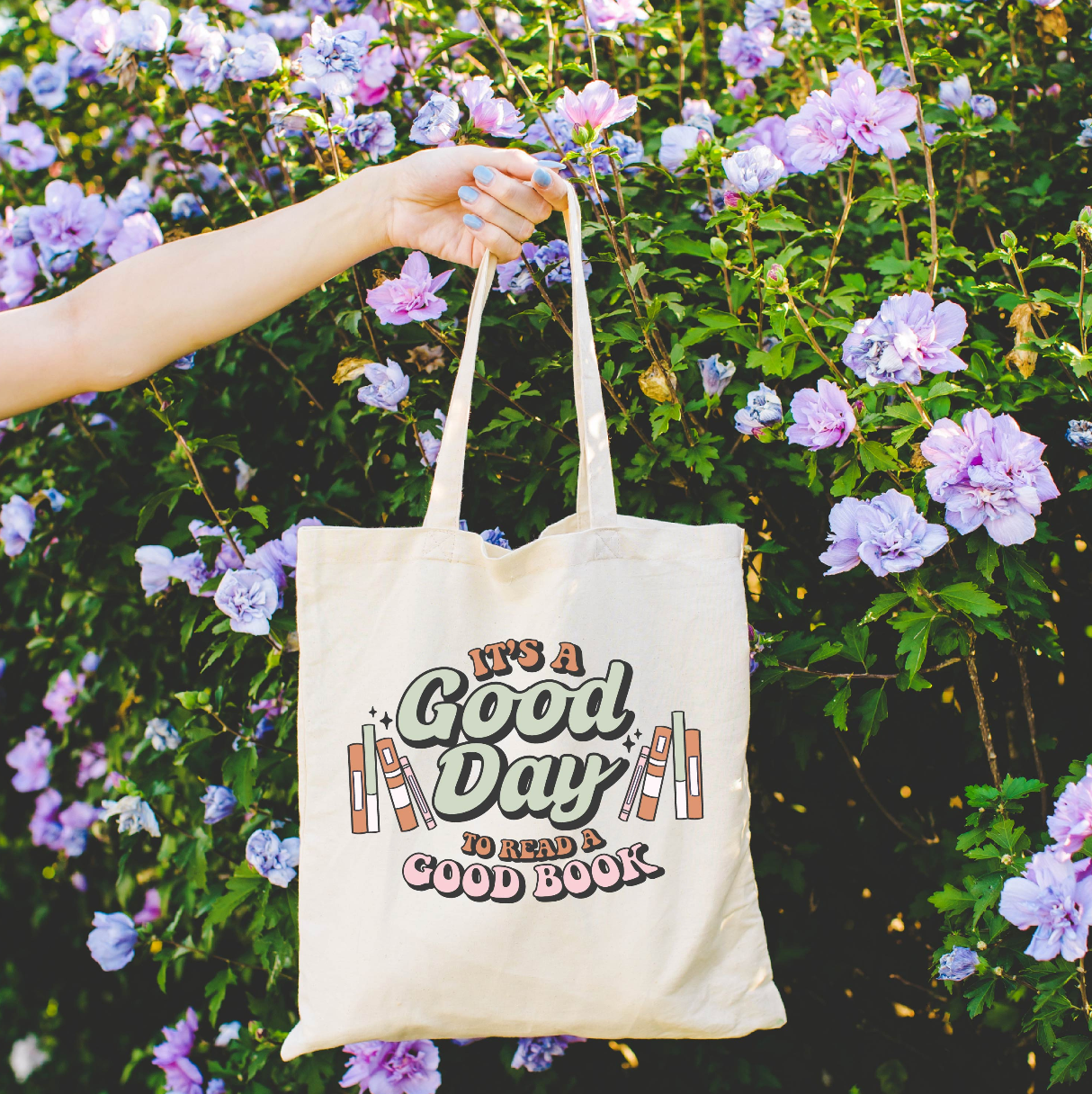 Beige canvas tote bag featuring a 'It's a good day to read a good book' design on a flat lay - Little Mama Shirt Shop