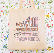 Beige canvas tote bag featuring a 'My weekend is booked' design on a flat lay - Little Mama Shirt Shop