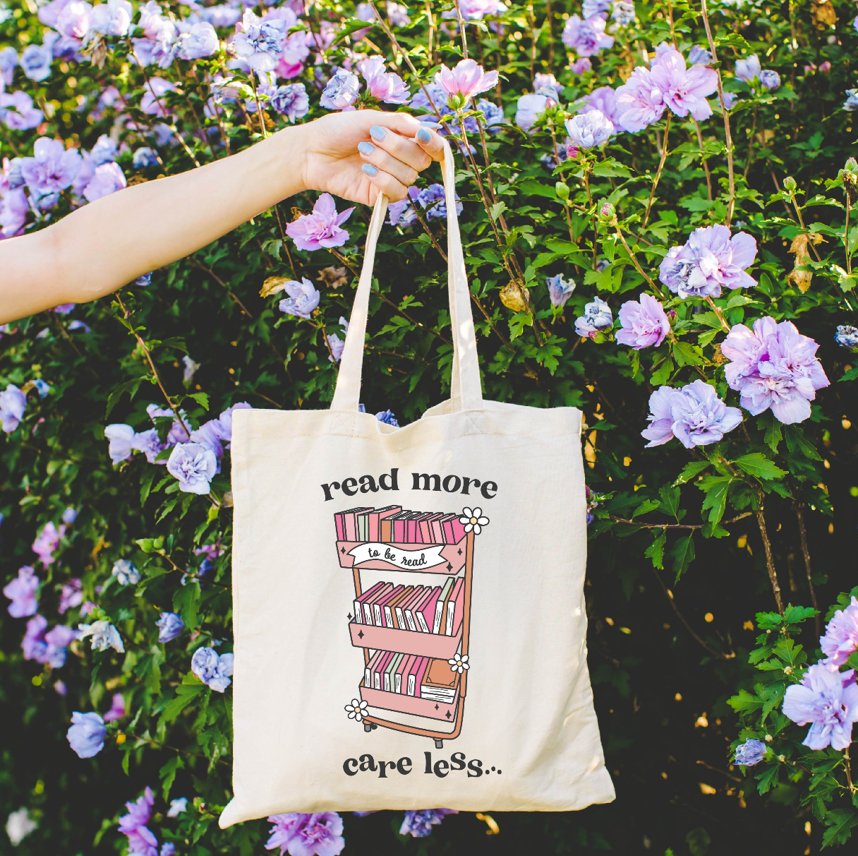 Beige canvas tote bag featuring a 'read more care less...' design on a flat lay - Little Mama Shirt Shop
