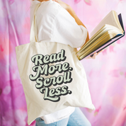 Beige canvas tote bag featuring a 'Read More. Scroll Less.' design on a model - Little Mama Shirt Shop
