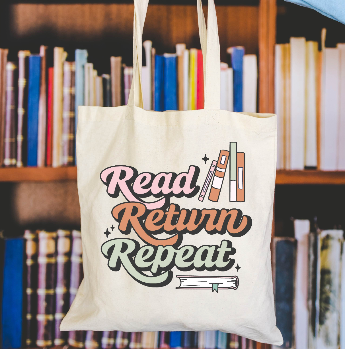 Beige canvas tote bag featuring a 'Read Return Repeat' design on a flat lay - Little Mama Shirt Shop
