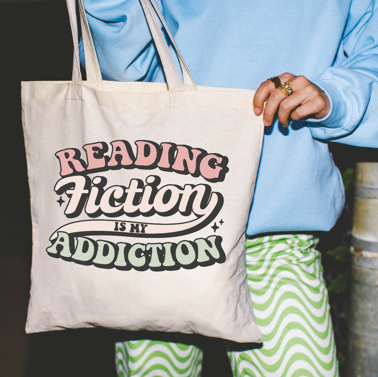 Beige canvas tote bag featuring a 'Reading Fiction is my Addiction' design on a model - Little Mama Shirt Shop