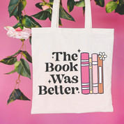 Beige canvas tote bag featuring a 'The Book Was Better' design on a flat lay - Little Mama Shirt Shop