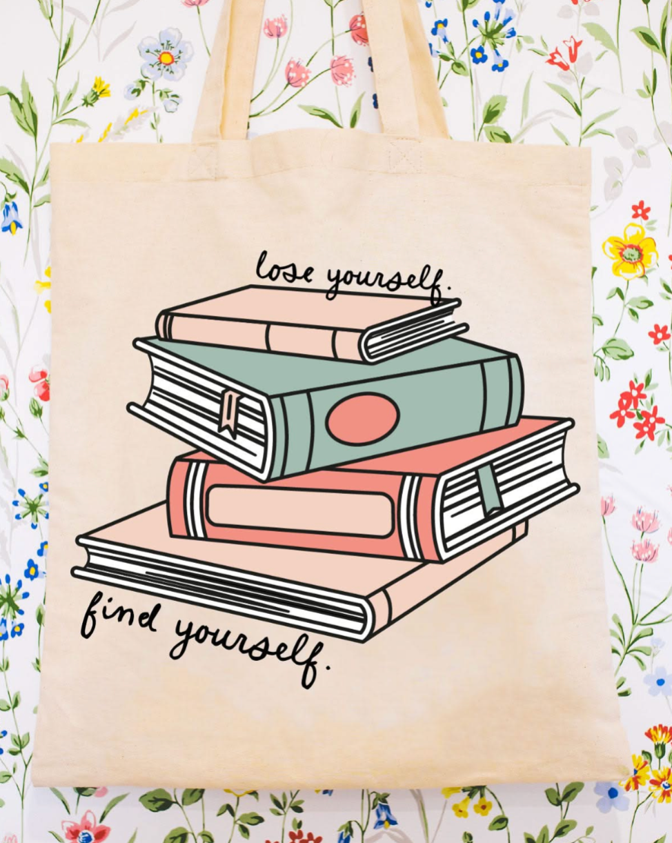 Beige canvas tote bag featuring a 'lose yourself. find yourself.' design on a flat lay - Little Mama Shirt Shop