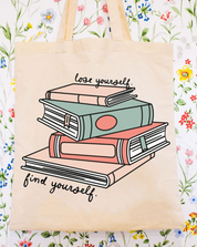 Beige canvas tote bag featuring a 'lose yourself. find yourself.' design on a flat lay - Little Mama Shirt Shop