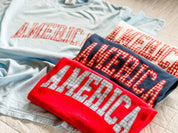 Close view of AMERICA shirts with gingham lettering, highlighting the texture and color contrast