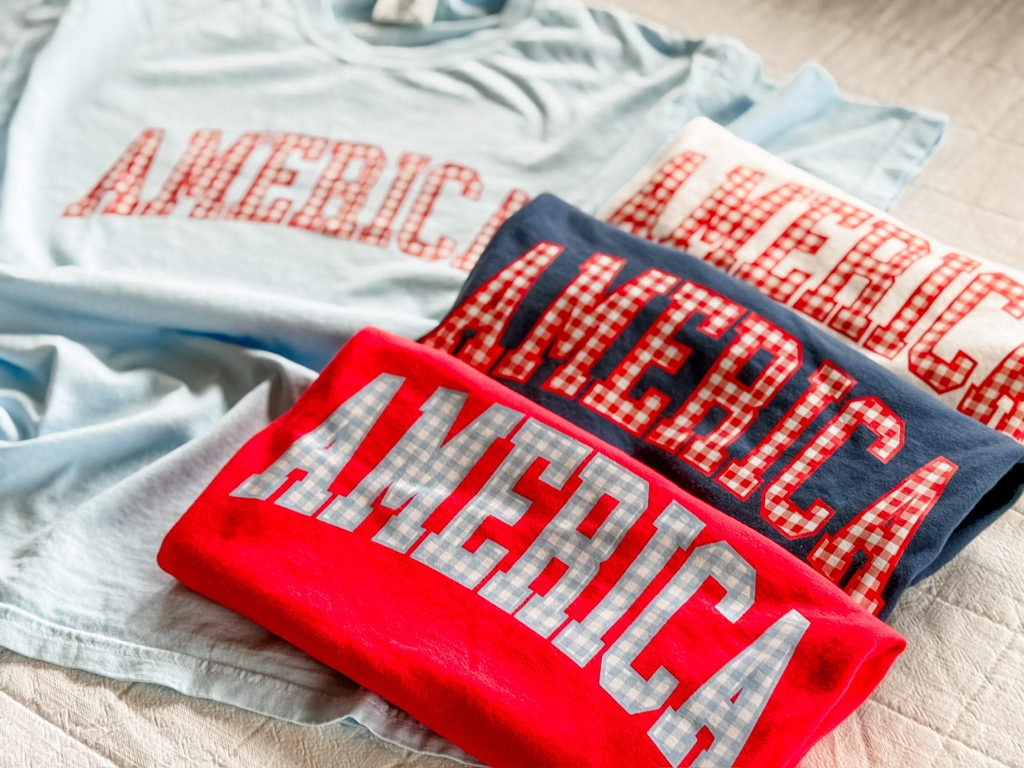Close view of AMERICA shirts with gingham lettering, highlighting the texture and color contrast