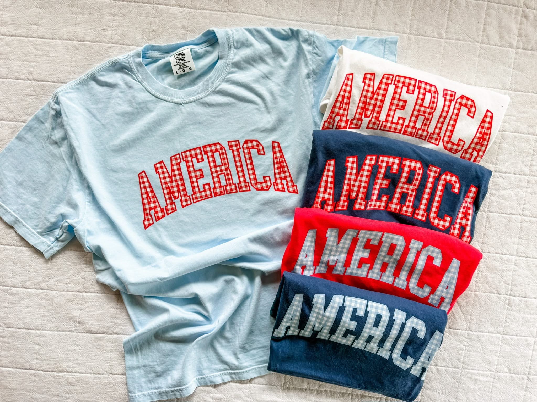 Red and blue AMERICA shirts with gingham print, displayed side by side in a simple flat lay