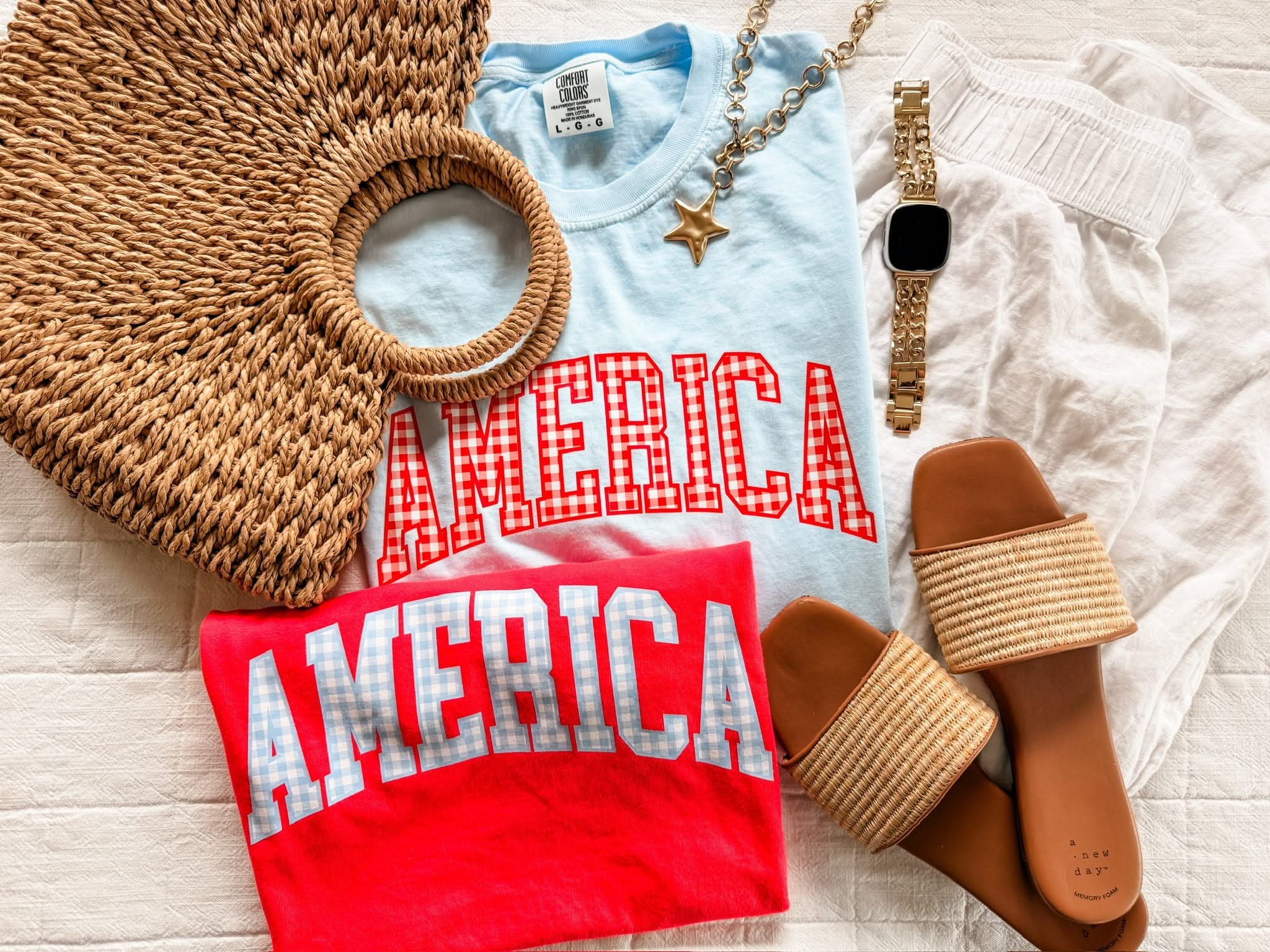 Red and blue AMERICA shirts with gingham print, displayed side by side with sandals, a woven, bag, and watch for a fun patriotic outfit idea