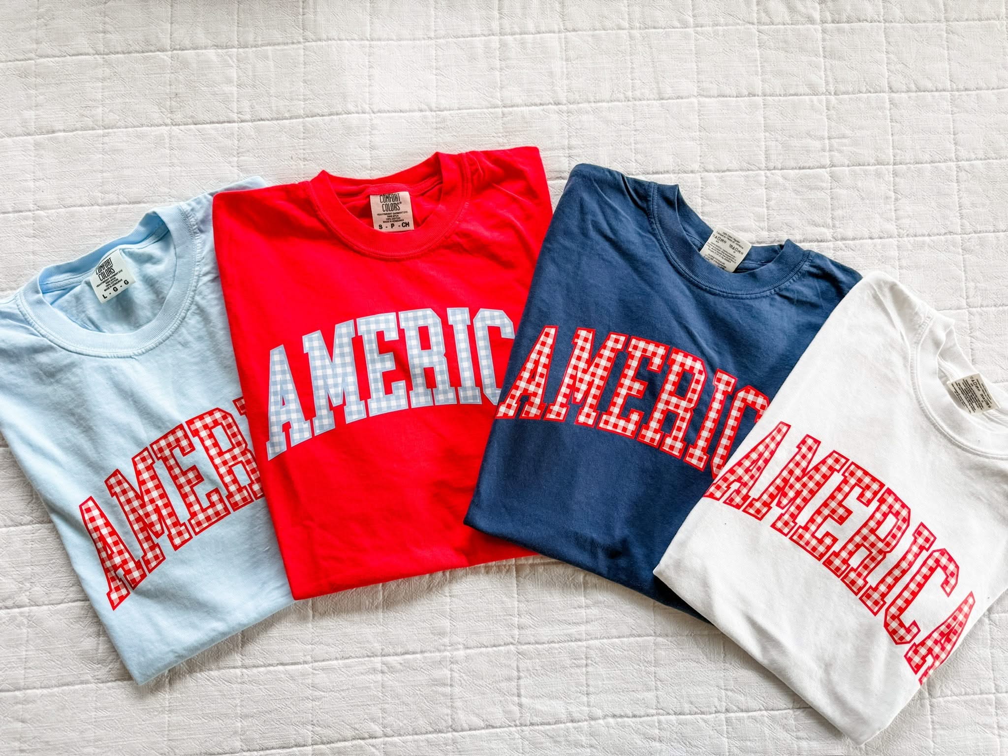 Comfort Colors AMERICA shirts in red, white, and blue with gingham lettering, laid out as a classic summer flat lay