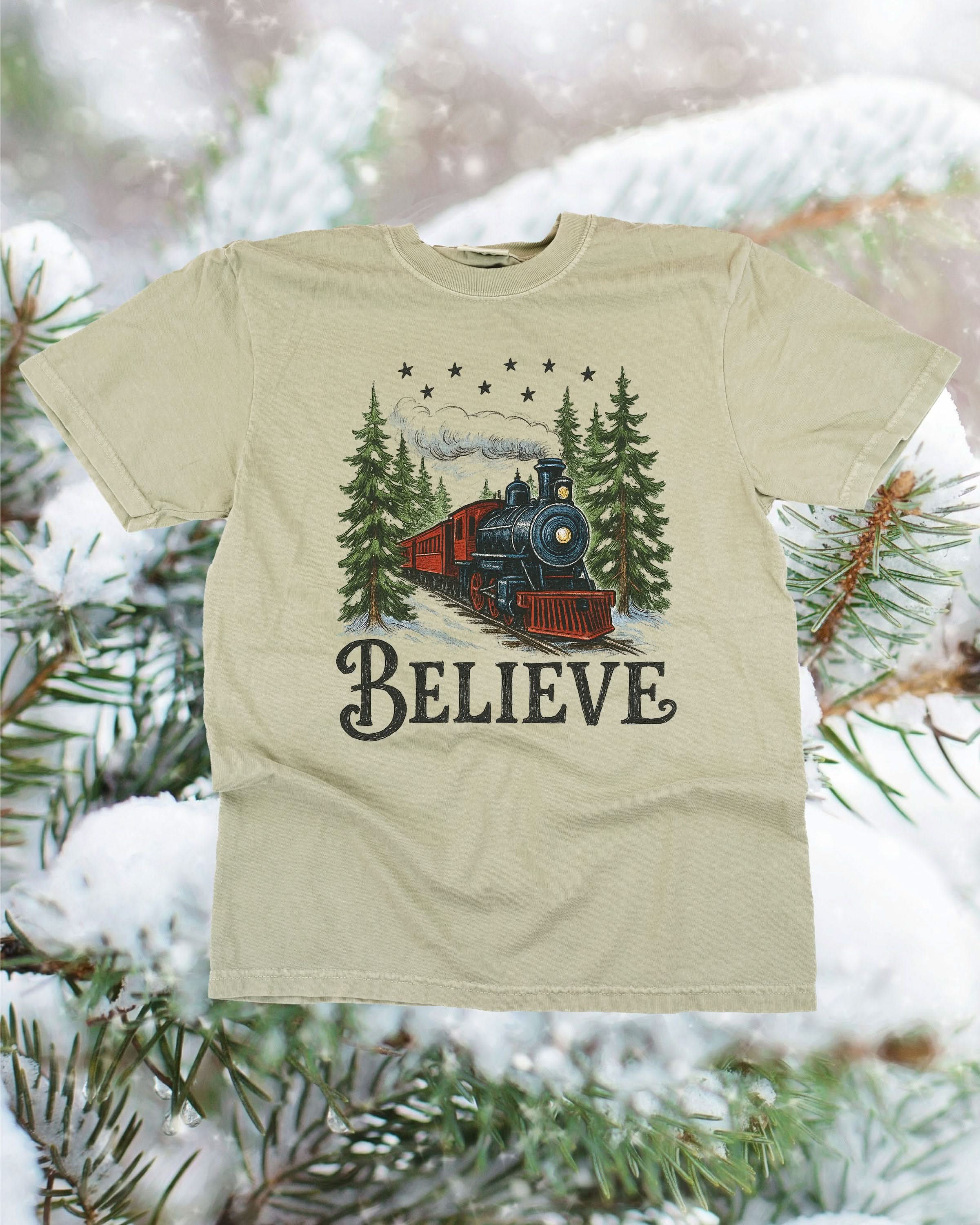 Comfort Colors Tee in sandstone with winter train and &#39;Believe&#39; on chest, shown on flat lay – Little Mama Shirt Shop