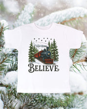 Child tee in white with winter train and 'Believe' on chest, shown on flat lay – Little Mama Shirt Shop
