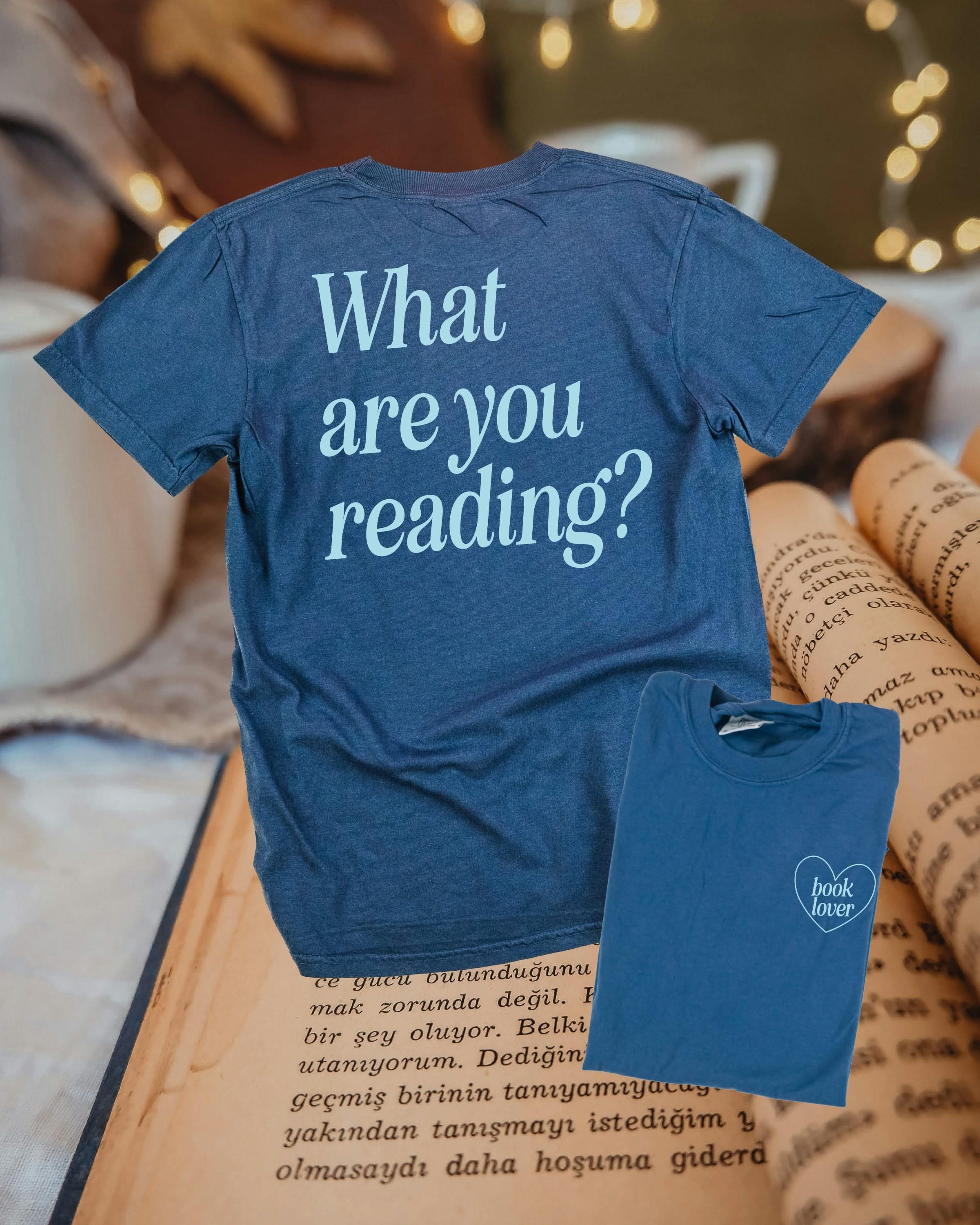Comfort colors tee in midnight navy w/ light blue detail with a 'book lover' heart graphic on the front and 'What are you reading?' graphic on back, shown on flat lay – Little Mama Shirt Shop