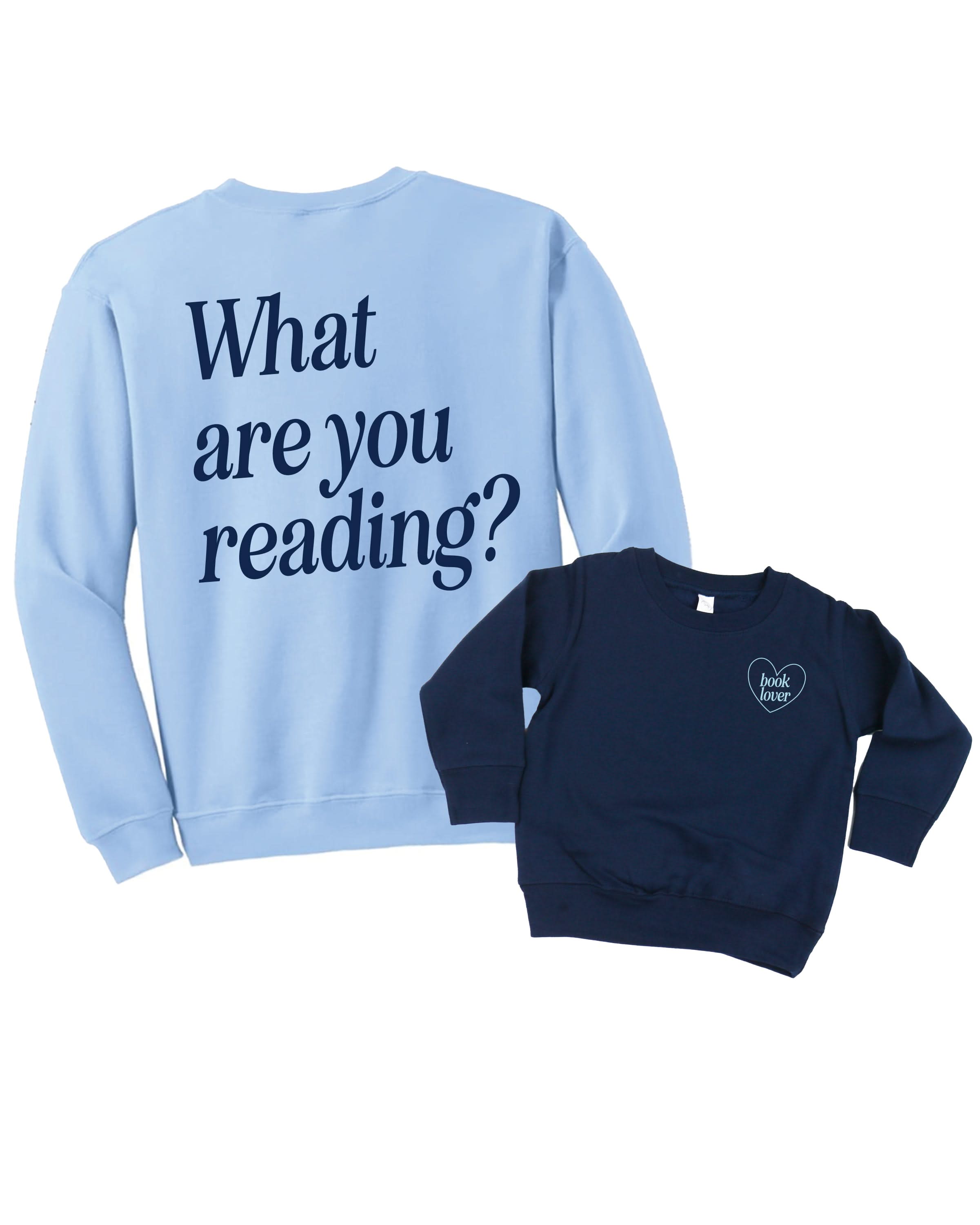 Set of two coordinating fleece sweaters for book lovers: an adult light blue sweater with navy “What are you reading?” text, paired with a child’s navy sweater with light blue “book lover” text in heart, displayed on side by side flat lay - Little Mama Shirt Shop