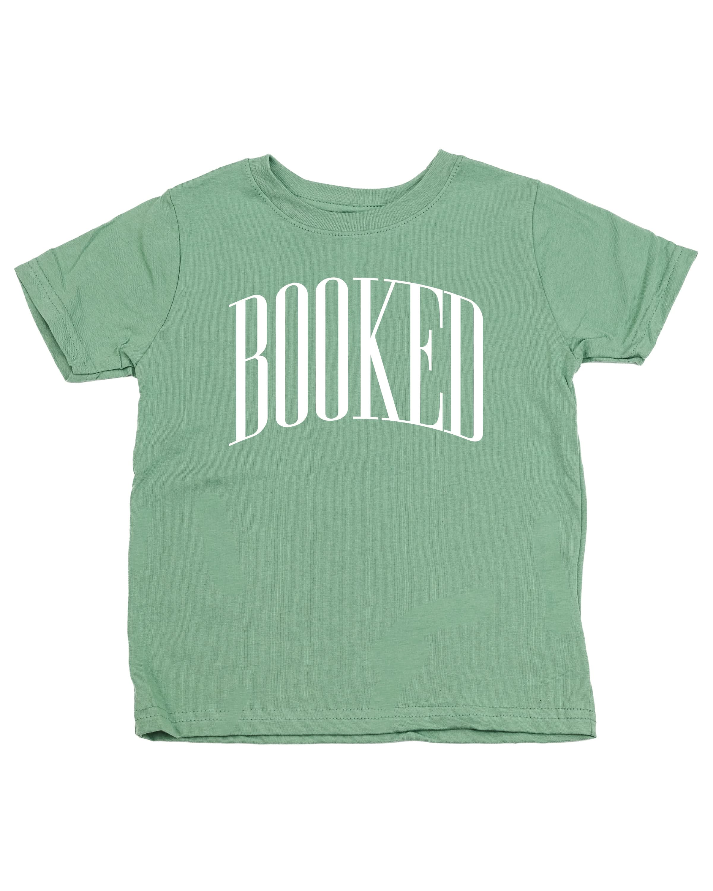 Child tee in sage with 'BOOKED' graphic on chest, shown on flat lay – Little Mama Shirt Shop
